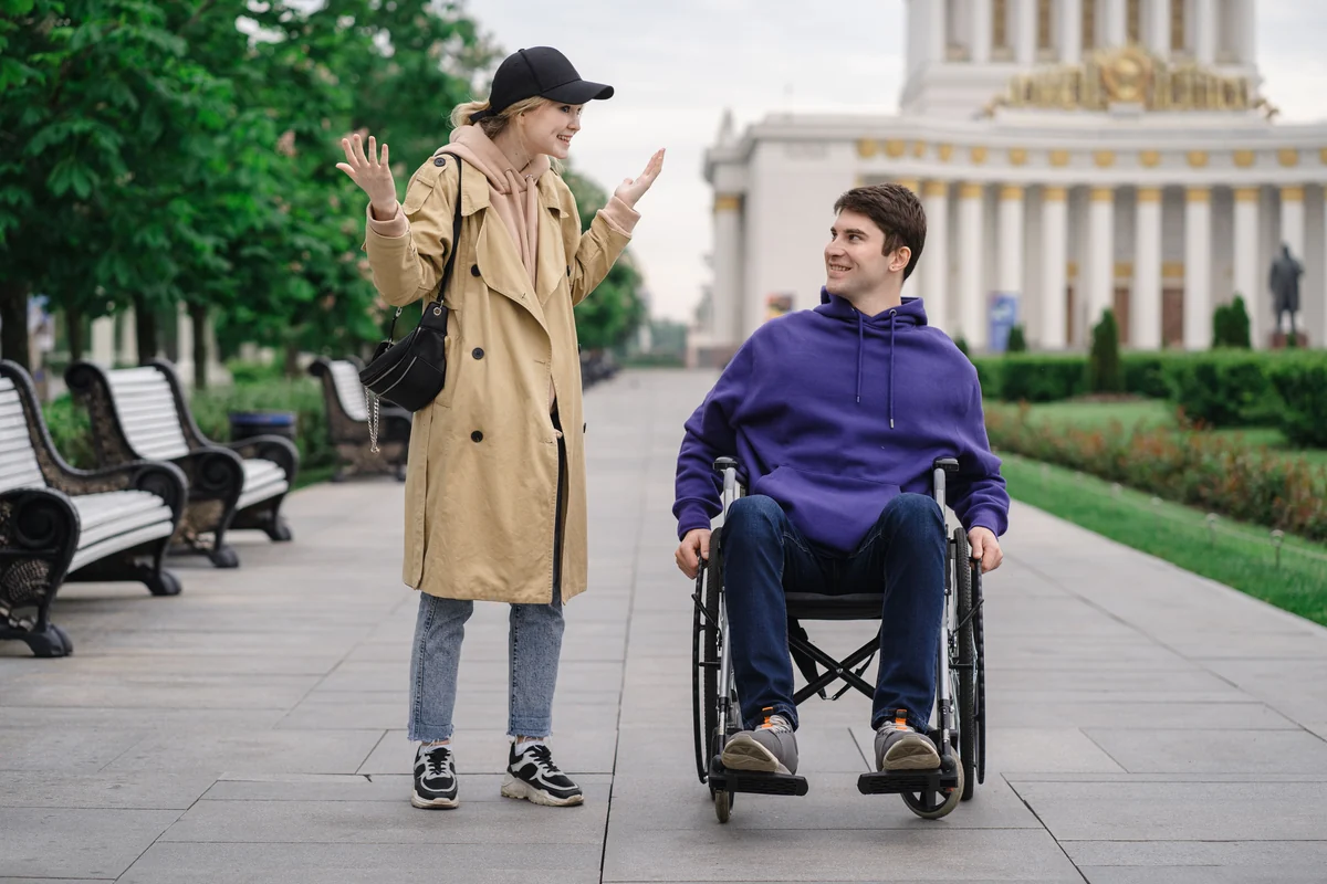 A woman and a man using a wheelchair sharing a conversation outdoors.